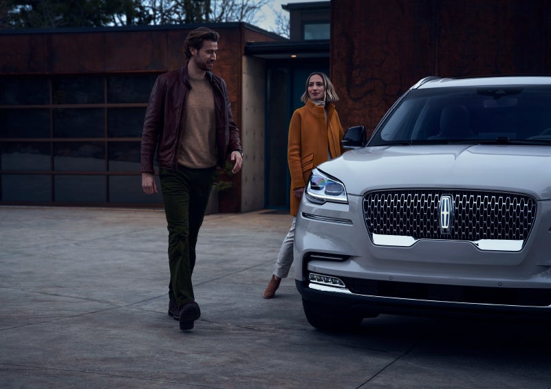 A man and a woman approaching a 2024 Lincoln Aviator® SUV, which illuminates certain lights when they are close | Eau Claire Lincoln in Eau Claire WI