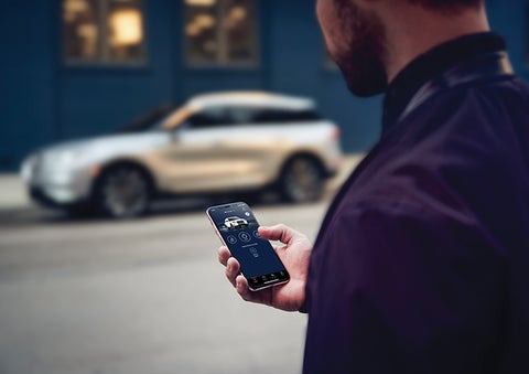 A person is shown interacting with a smartphone to connect to a Lincoln vehicle across the street. | Eau Claire Lincoln in Eau Claire WI