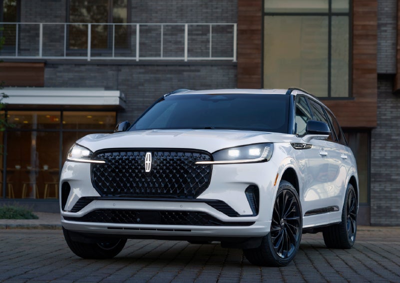 A 2026 Lincoln Aviator® Reserve model is shown with the available Jet Appearance Package parked near a restaurant. | Eau Claire Lincoln in Eau Claire WI