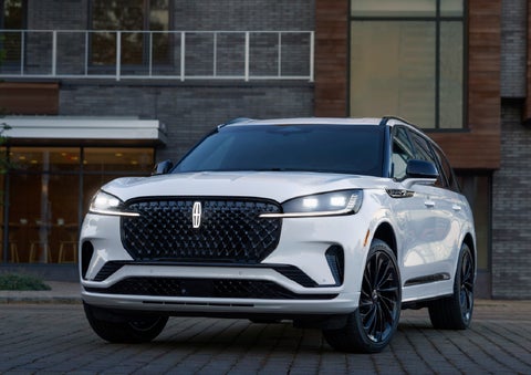 A 2026 Lincoln Aviator® Reserve model is shown with the available Jet Appearance Package parked near a restaurant. | Eau Claire Lincoln in Eau Claire WI