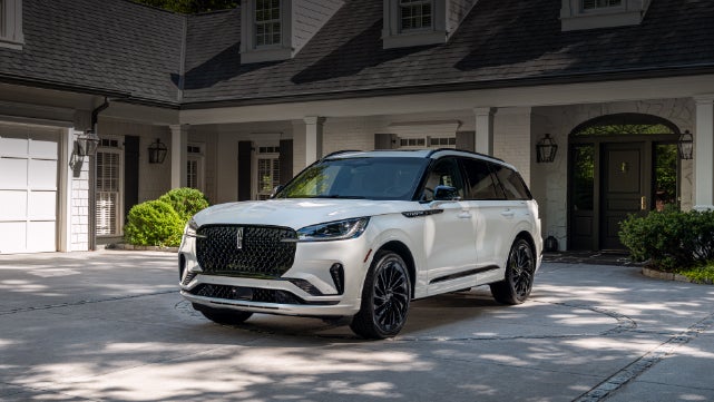 A white 2026 Lincoln Aviator® SUV is parked in the driveway of a luxury home. | Eau Claire Lincoln in Eau Claire WI